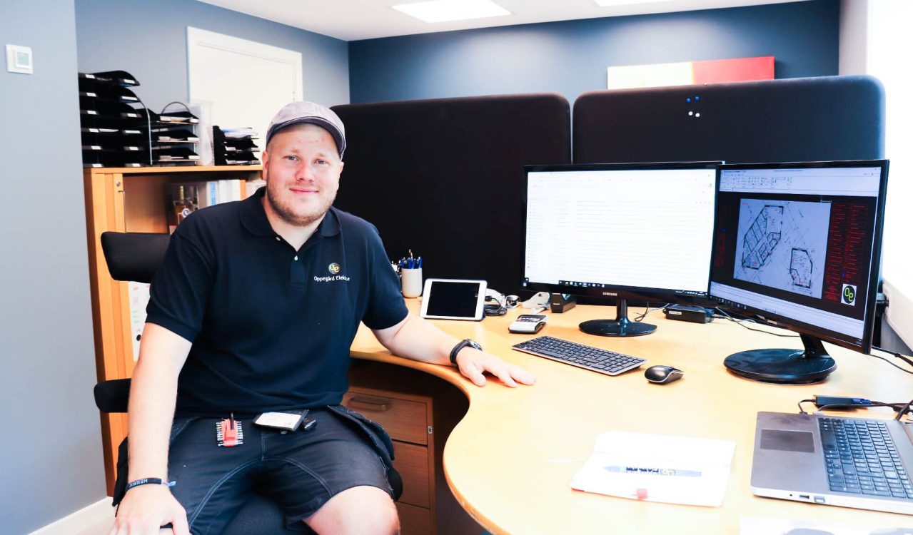 Elektroinstallatør Henrik Aasen i Oppegård Elektriske sitter ved kontorpult med PC-skjermer som viser arbeidstegninger.